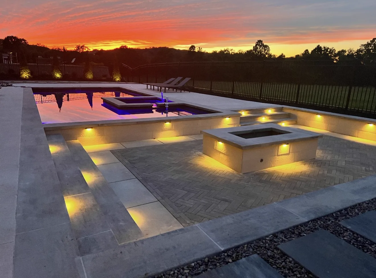 Custom pool with fire features and paver patio glowing at sunset in a Middle Tennessee backyard